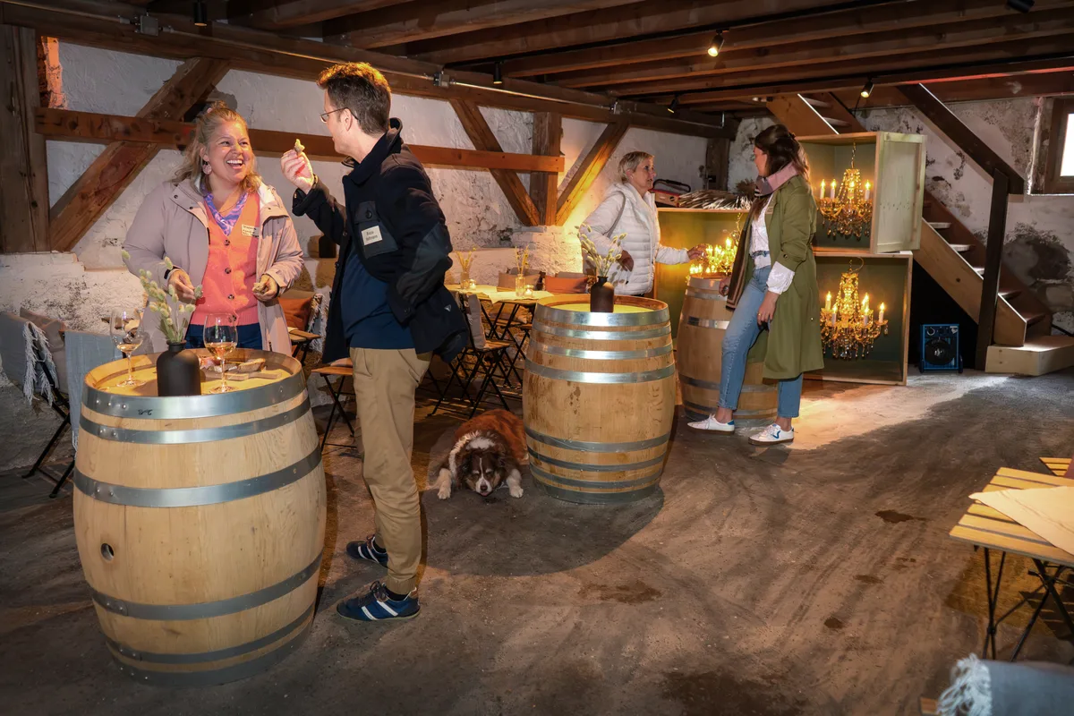 Menschen unterhalten sich in einem rustikalen Raum. Grosse Weinfässer dienen als Tische.